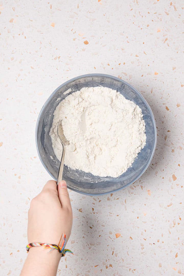 A hand preparing dough for an Easy Cherry Pie in a grey bowl with a fork on a speckled countertop.