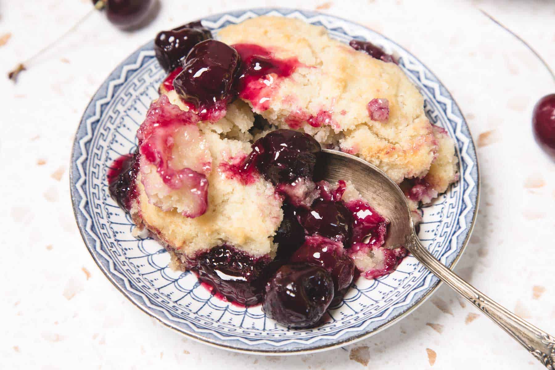 A plate with Cherry Pie Casserole and a spoon, featuring juicy cherries and a golden biscuit topping&mdash;an easy recipe for dessert lovers.