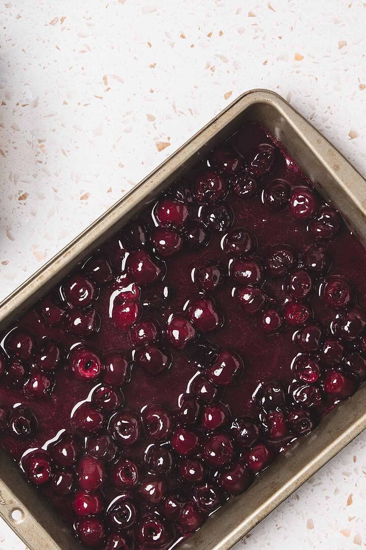 A baking pan filled with glossy cherry pie filling sits on a white countertop, perfect for an easy recipe.