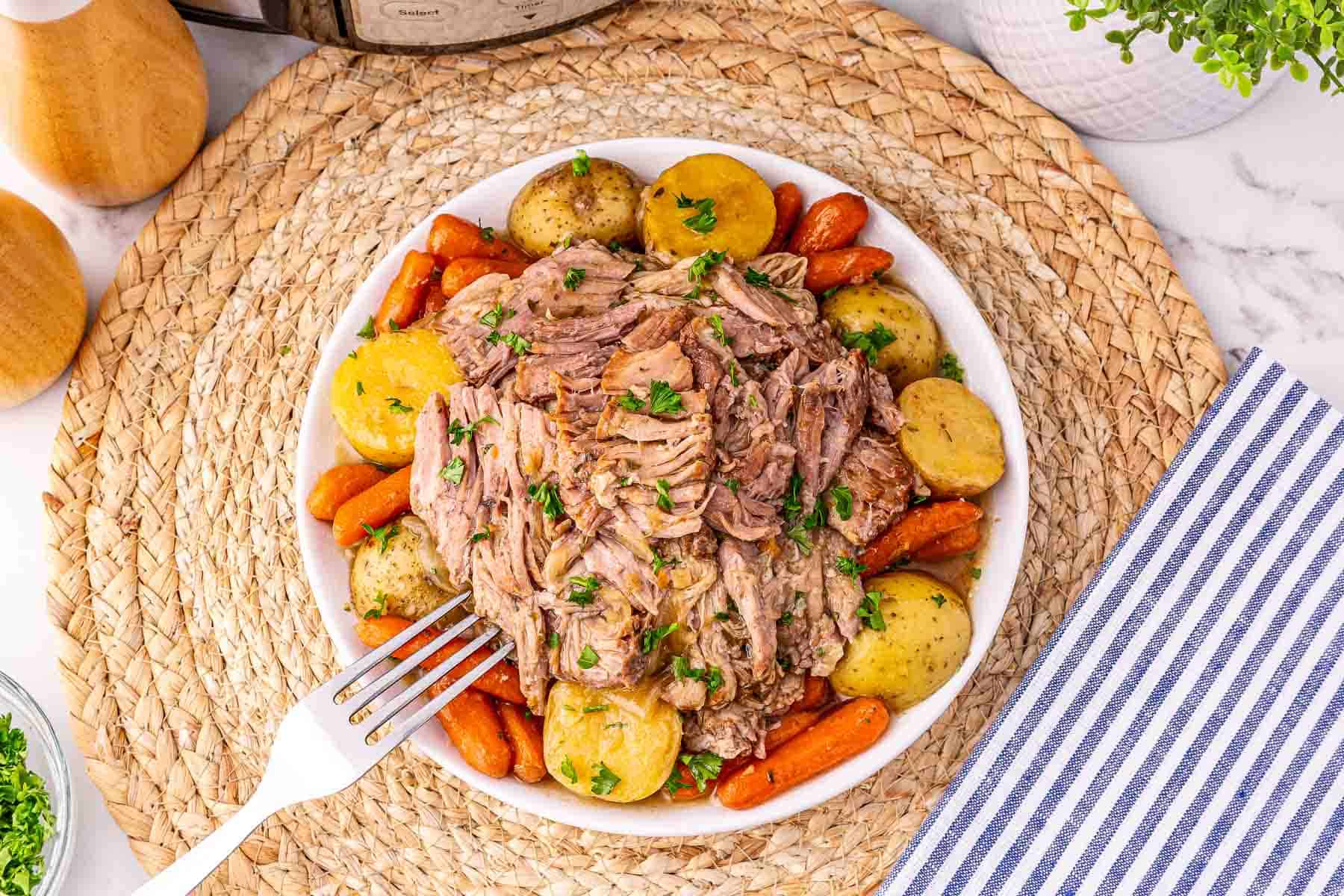 A bowl of Crock Pot Pork Roast with shredded beef, baby potatoes, and carrots, garnished with parsley.