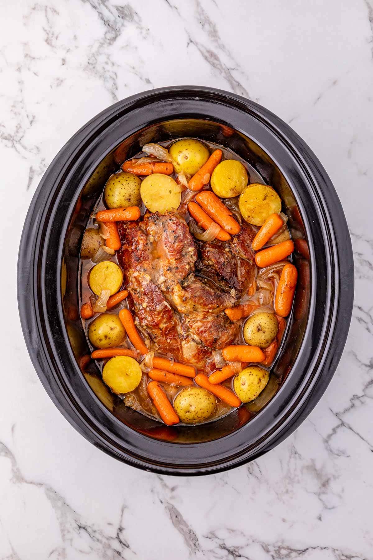 Easy Pork Roast with baby potatoes and carrots in a Crock Pot, set on a marble countertop.