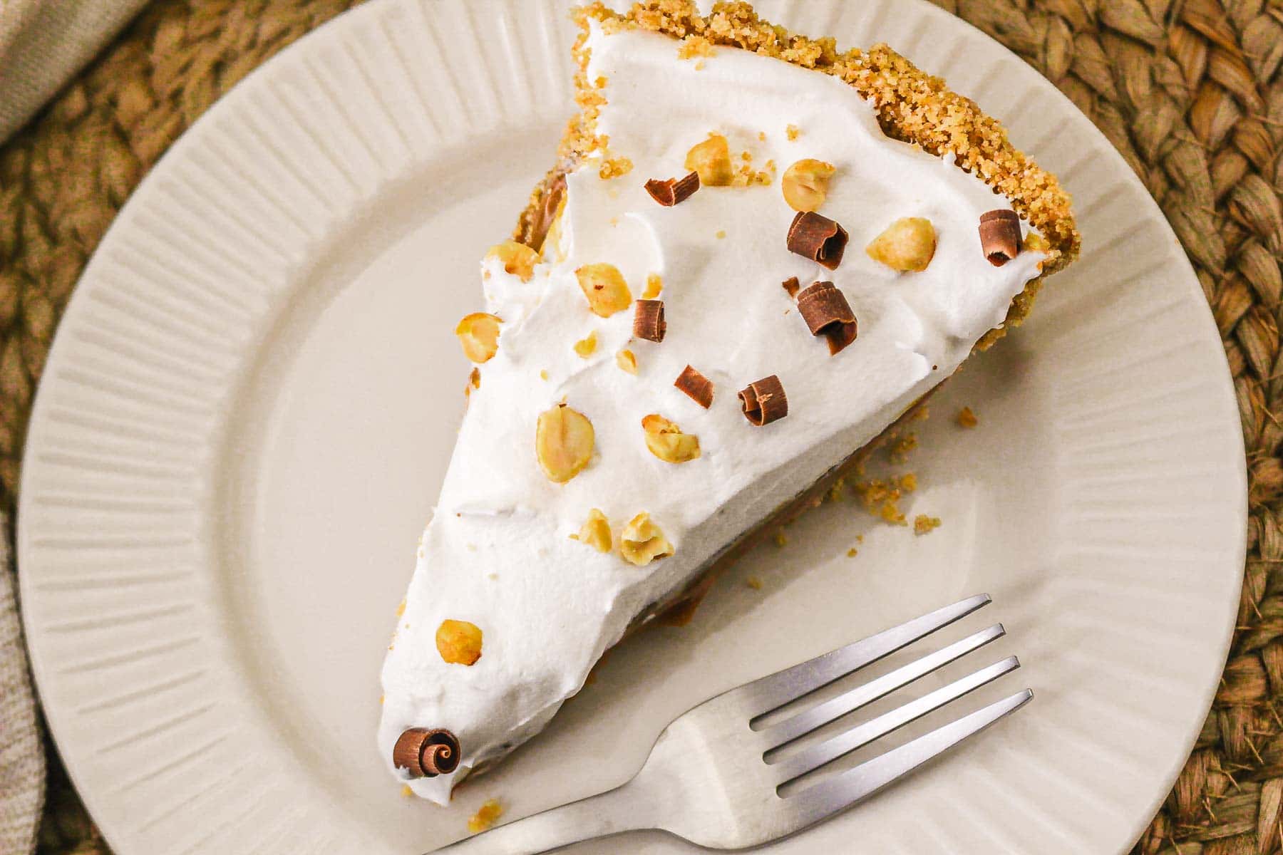 A slice of caramel pie with nuts and chocolate curls on top, served on a white plate with a fork—an indulgent recipe perfect for any occasion.