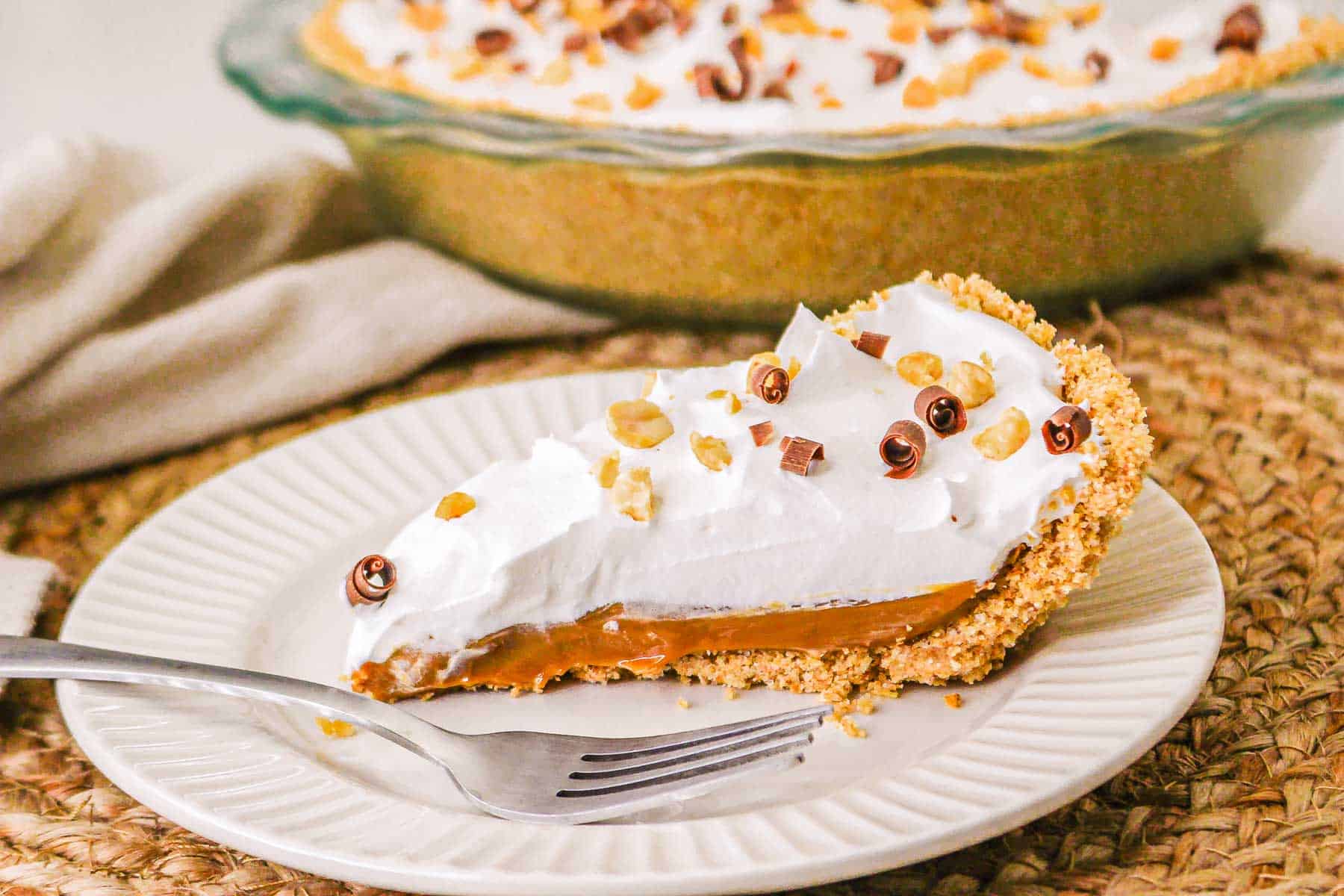 A slice of Caramel Pie with whipped cream and chocolate shavings on a plate, with a fork beside it—try this easy recipe for the perfect dessert.