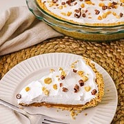 A slice of caramel pie with whipped topping, nuts, and chocolate curls on a plate with a fork—try this irresistible recipe for a luscious dessert everyone will love.