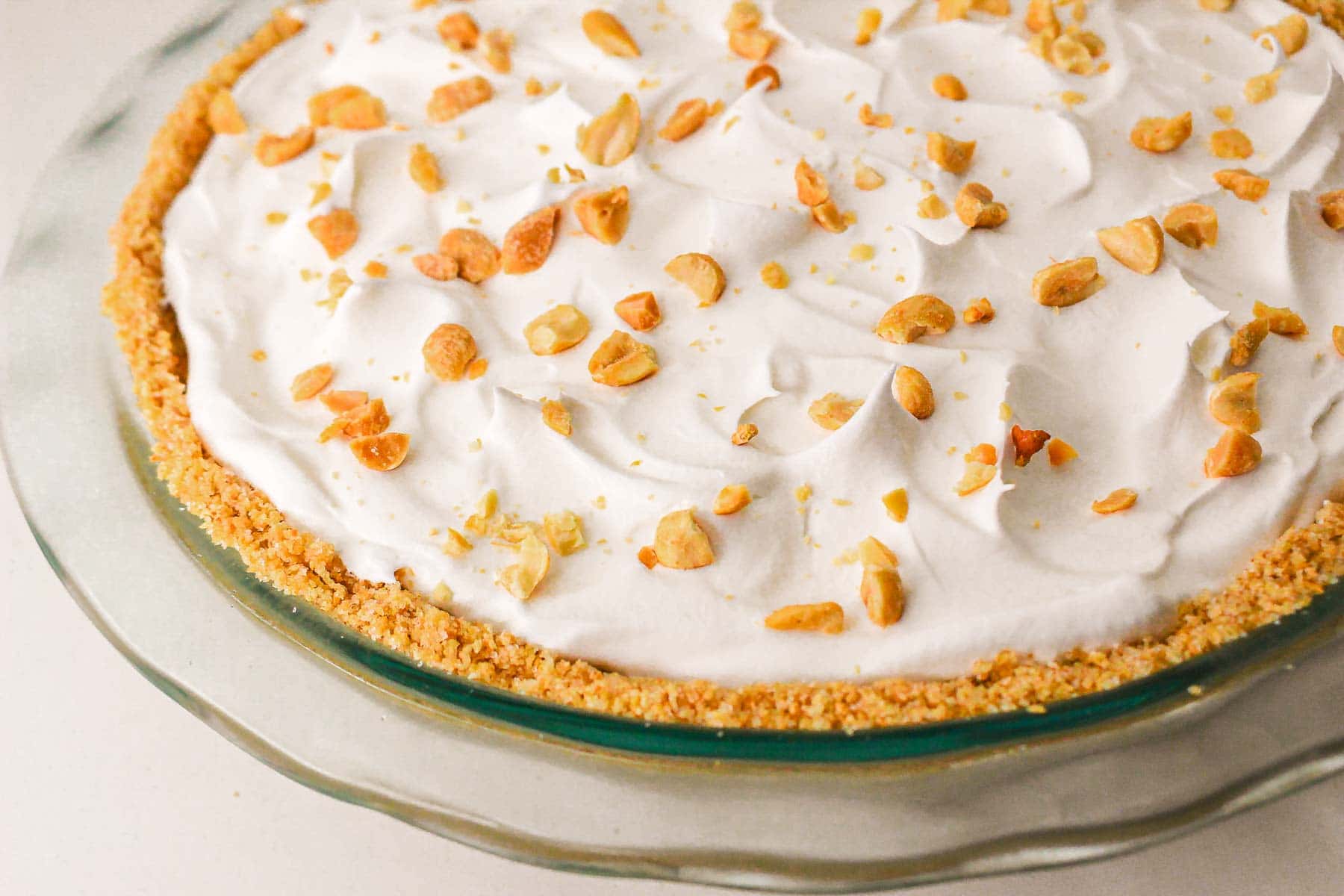 A caramel pie with a crumb crust, topped with whipped cream and chopped peanuts in a glass pie dish—this recipe is sure to satisfy any sweet tooth.