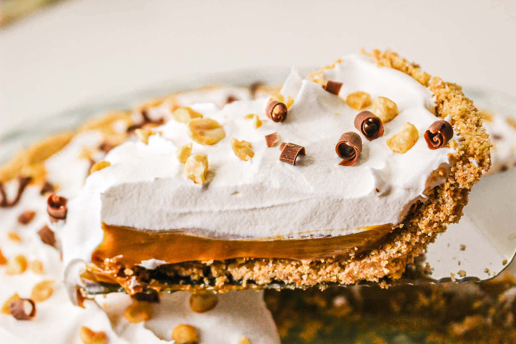 A slice of slow cooker caramel pie with whipped cream, rich caramel filling, and sprinkled nuts and chocolate curls on top.