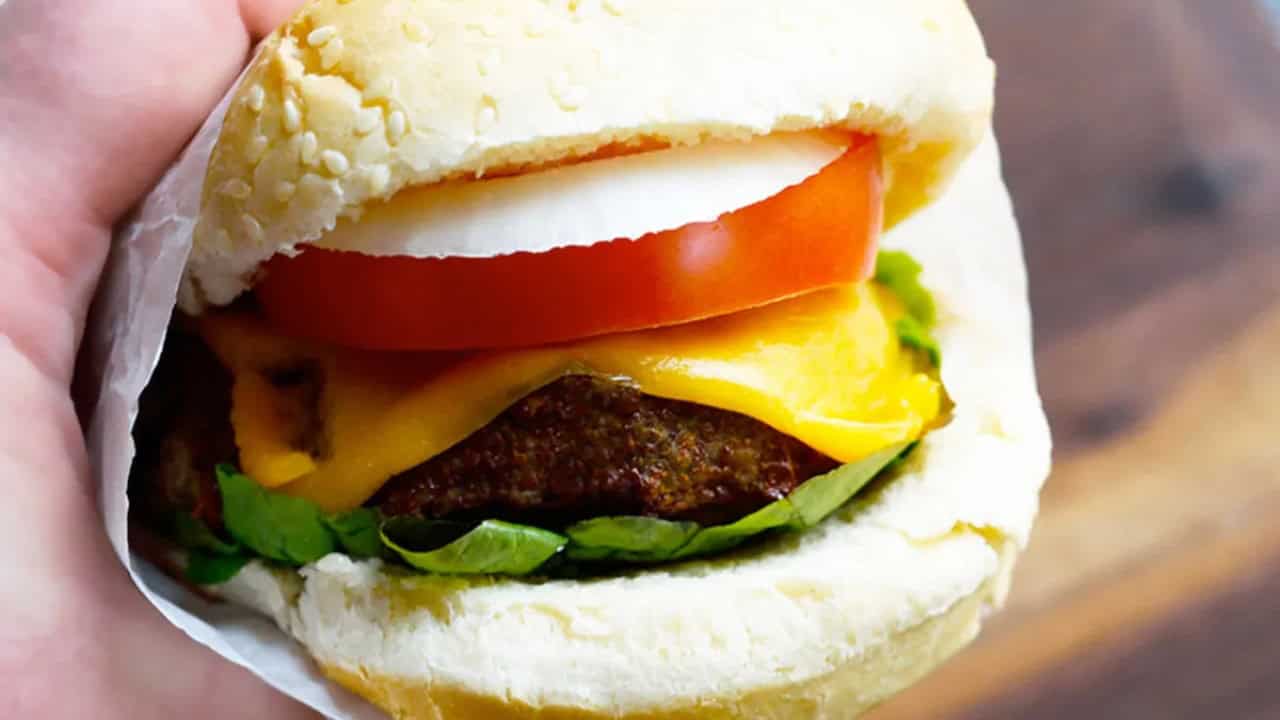 Hand holding an air fryer turkey burger wrapped in tissue, showing onion, tomato, cheese, lettuce, and meat inside.