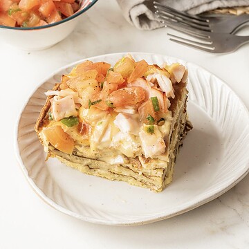 A slice of Pancake Breakfast Casserole topped with diced tomatoes and herbs sits on a white plate.