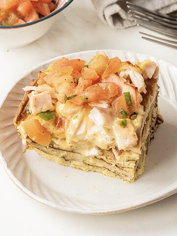 A slice of Pancake Breakfast Casserole topped with diced tomatoes and herbs sits on a white plate.
