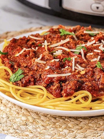 A plate of Spaghetti Bolognese topped with meat sauce, grated cheese, and parsley sits on a woven placemat.