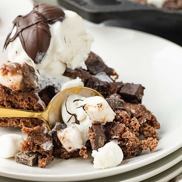A close-up of a decadent Hot Chocolate Cobbler with ice cream, marshmallows, and a gold spoon on a white plate.
