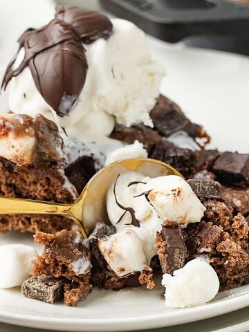 A close-up of a decadent Hot Chocolate Cobbler with ice cream, marshmallows, and a gold spoon on a white plate.