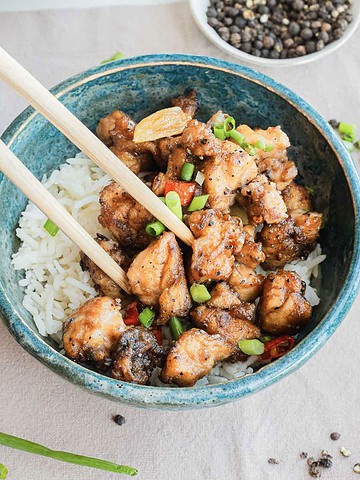 A bowl of rice topped with stir-fried chicken and chopped green onions, held with chopsticks.