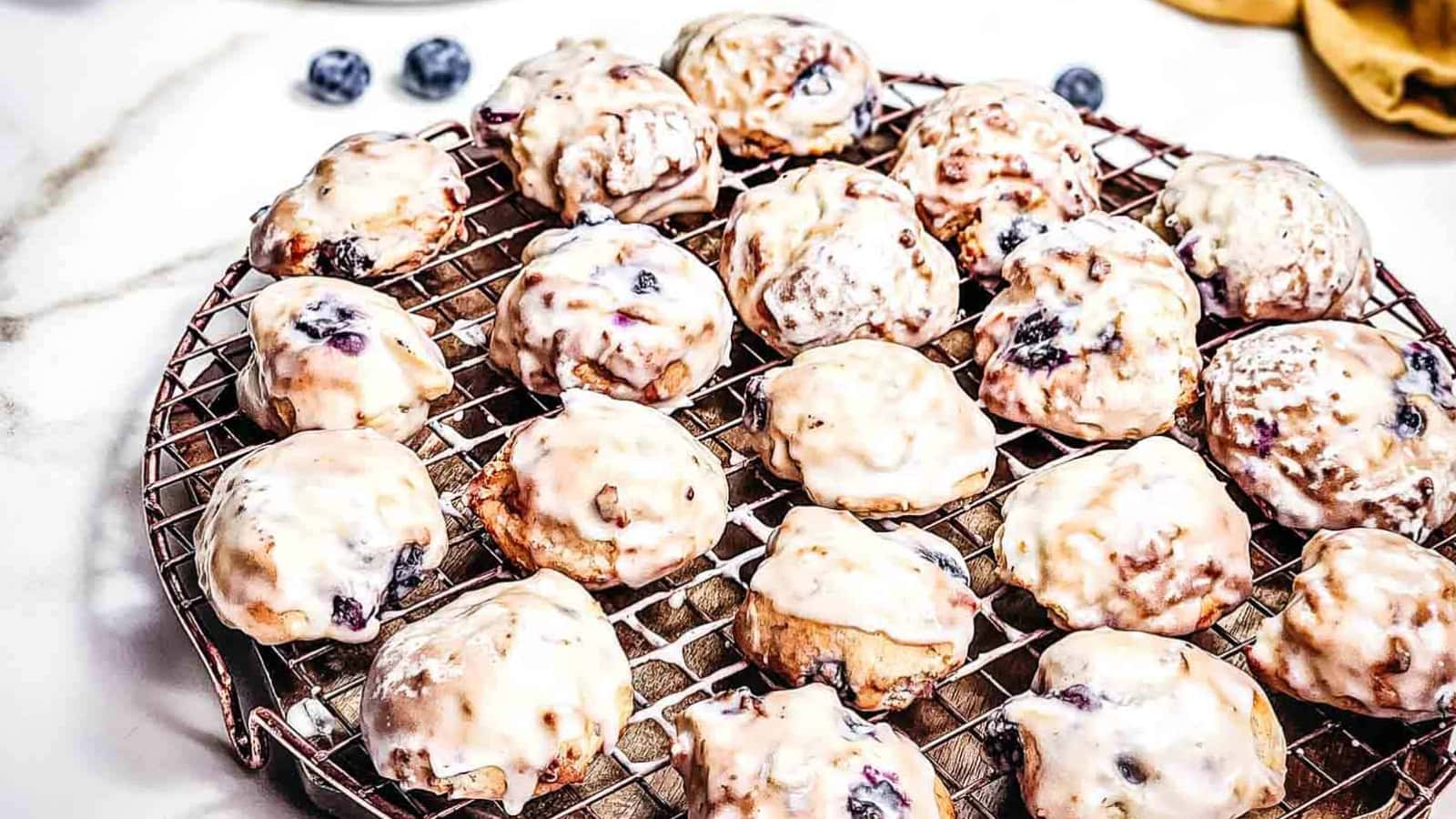 Iced blueberry cookies cooling on a wire rack, with some fresh blueberries in the background.
