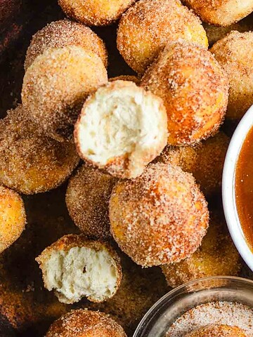 Round cinnamon sugar donuts on a plate with caramel dipping sauce and a bitten donut on top.