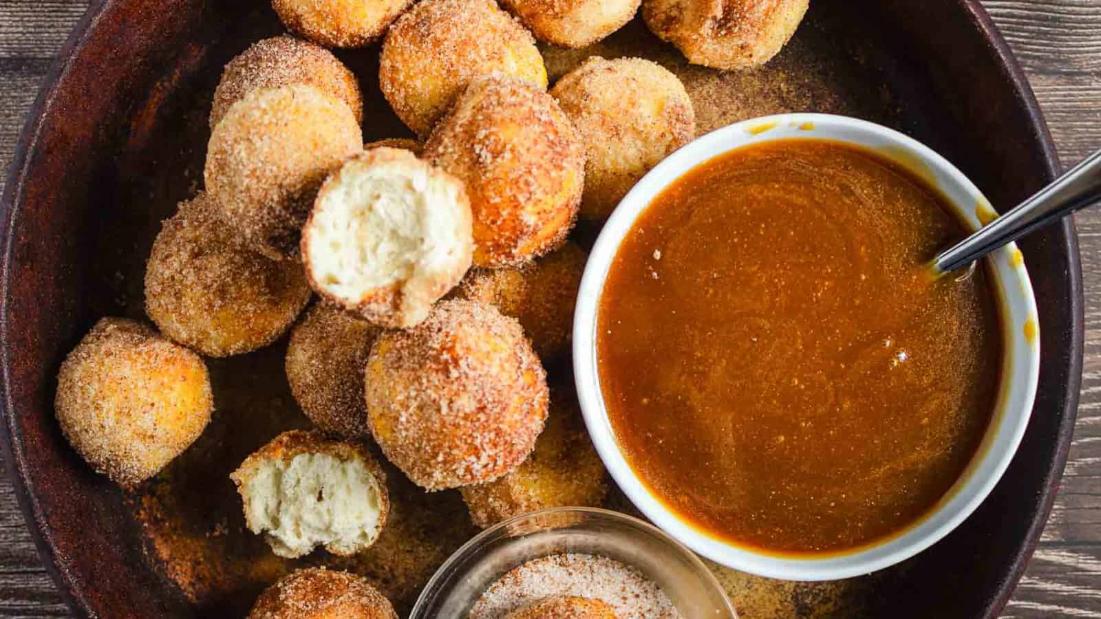 Cinnamon sugar donut holes with a caramel dipping sauce in a bowl on a dark plate.