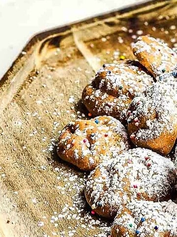 A pile of powdered sugar cookies with colorful sprinkles on a wooden tray.