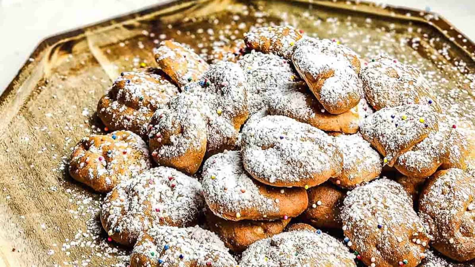 A pile of powdered sugar-covered cookies with colorful sprinkles on a wooden tray.