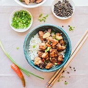 A bowl of rice topped with seasoned air fryer chicken, surrounded by chopped onions, peppers, and black peppercorns.