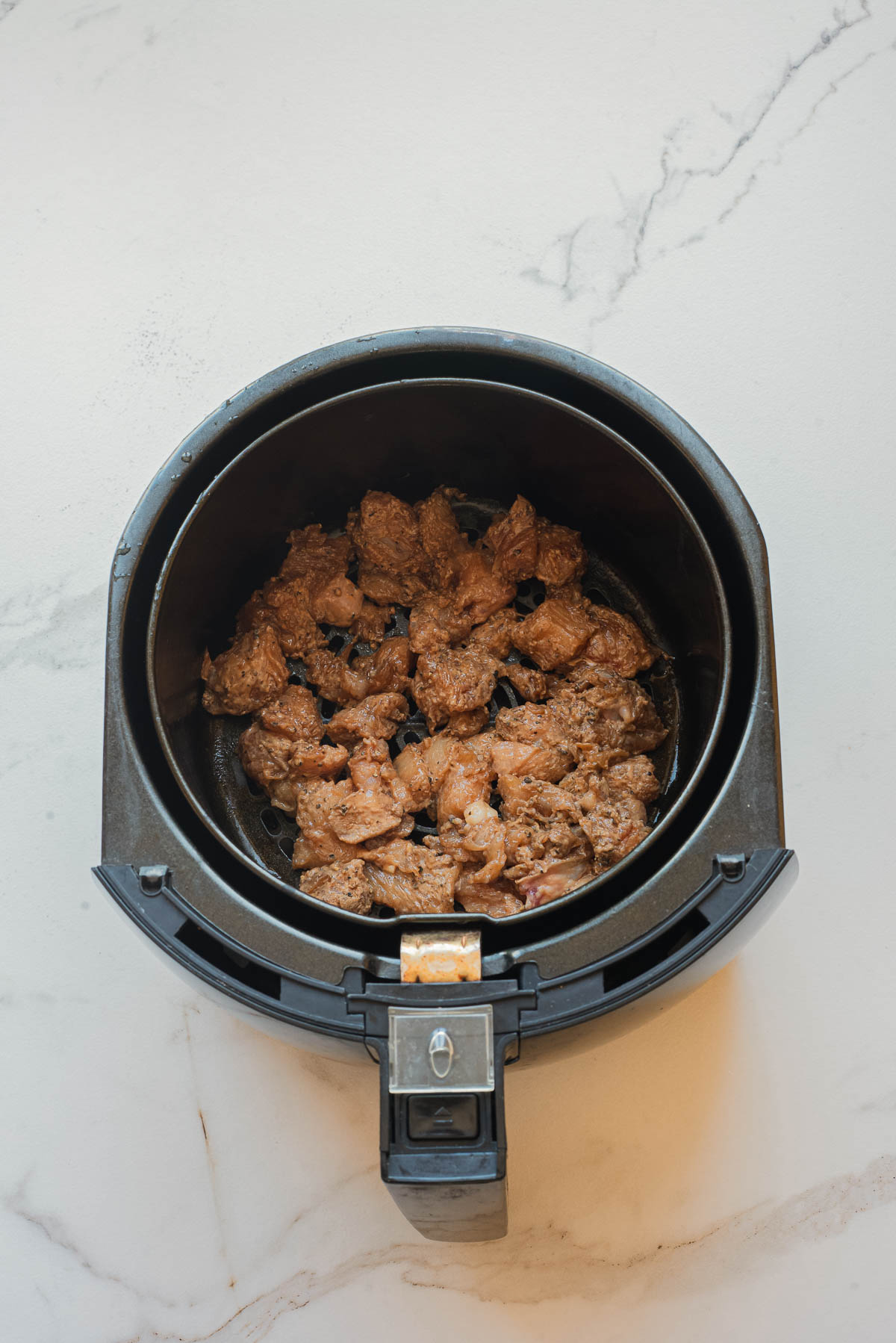Salt and Pepper Chicken recipe featuring cooked marinated meat pieces in a black air fryer basket on a white marble surface.