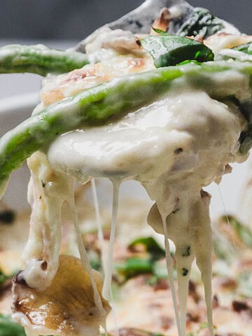 A spoon lifts green beans covered in creamy, melted cheese from a casserole dish.