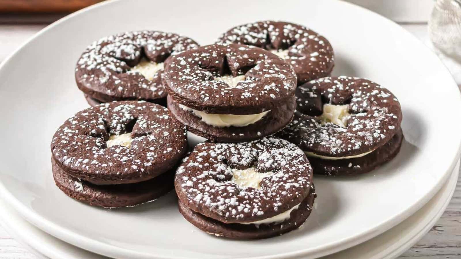 Seven chocolate sandwich cookies with cream filling and powdered sugar on a white plate.