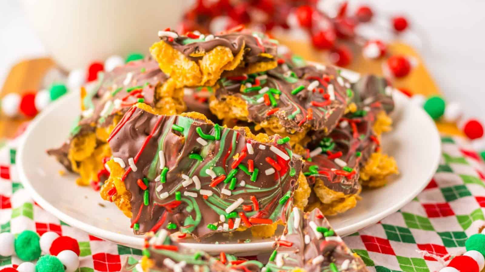 Chocolate bark with red, green, and white sprinkles on a plate, festive decorations in the background.