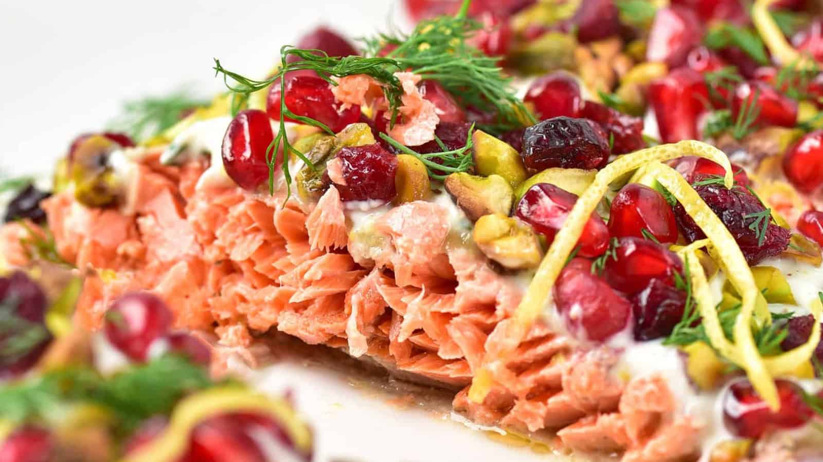 Close-up of cooked salmon topped with pomegranate seeds, pistachios, dill, and lemon zest.