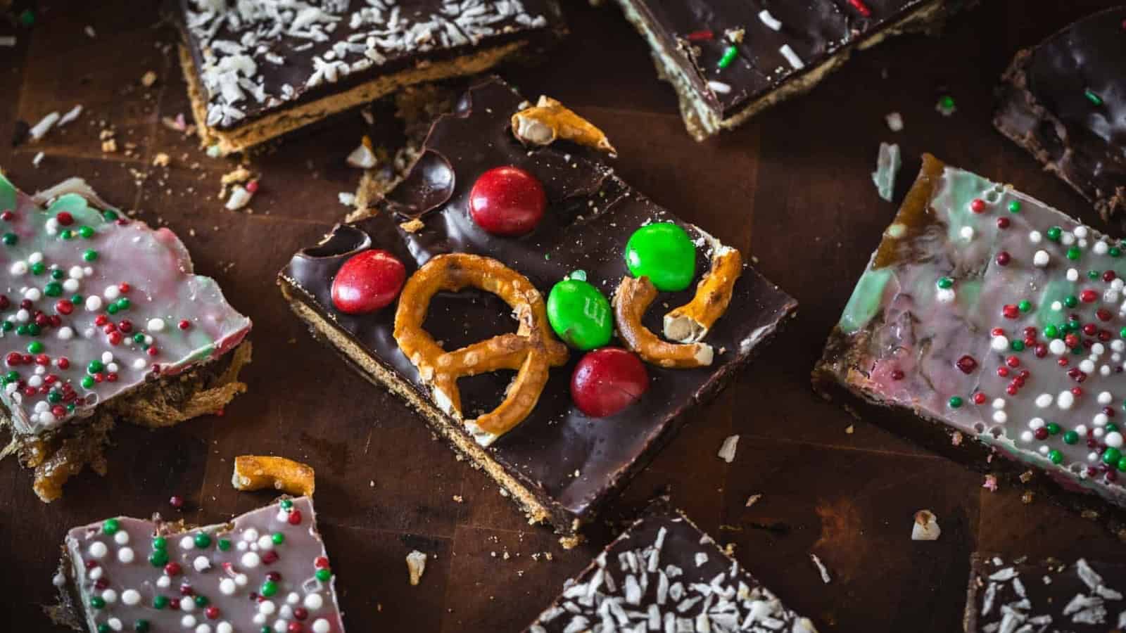 Chocolate bark topped with pretzels, red and green candies, and holiday-themed sprinkles on a wooden surface.