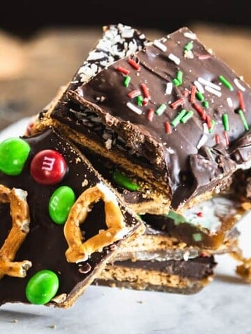 Stack of chocolate bark topped with pretzels, green and red candies, and holiday sprinkles on parchment paper.