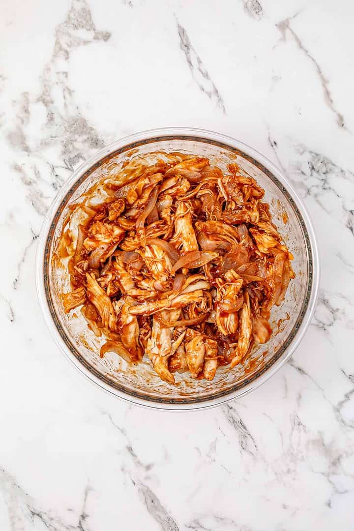 A glass bowl of shredded jackfruit mixed with barbecue sauce on a white marble surface, perfect for making flavorful BBQ Sliders.