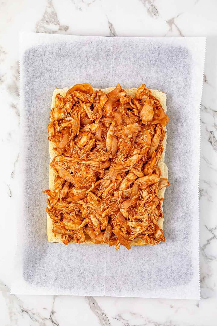 Rectangular flatbread topped with shredded barbecue chicken, perfect for making easy BBQ Chicken Sliders, served on parchment paper atop a marble surface.