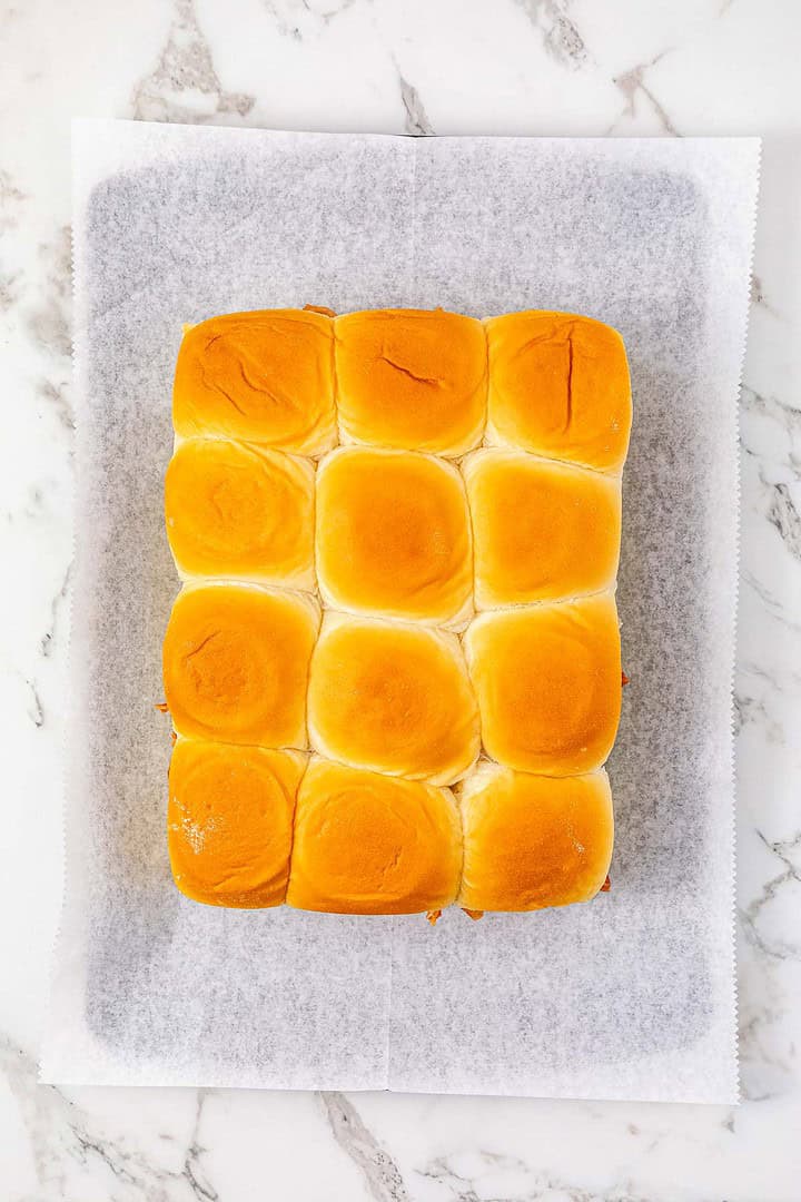 Twelve golden brown BBQ Chicken Sliders arranged in a 4x3 grid on parchment paper on a marble surface, perfect for serving up easy BBQ chicken at your next gathering.