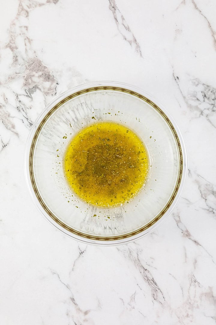 A glass bowl with yellow vinaigrette dressing on a white marble surface, perfect for drizzling over BBQ Chicken Sliders or Easy Chicken Sliders.