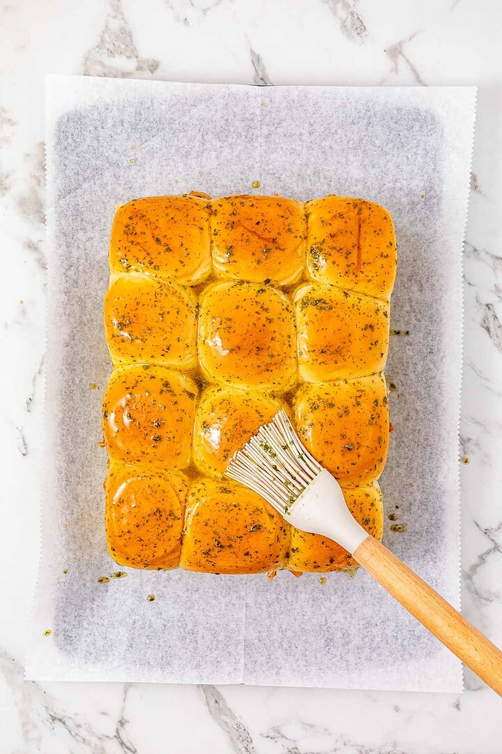 Golden dinner rolls brushed with herb butter, perfect for serving as easy chicken sliders or alongside your favorite BBQ sliders, arranged on parchment paper over a marble surface.