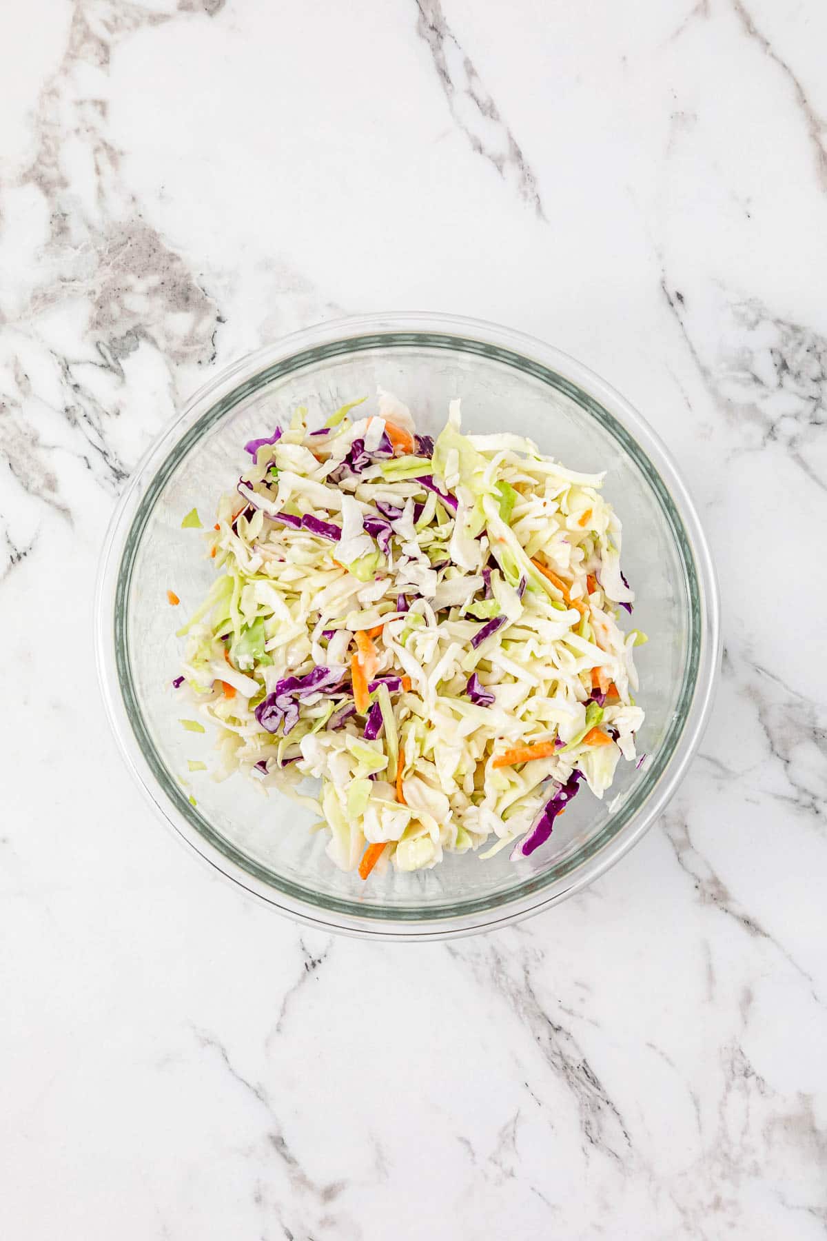 A glass bowl filled with shredded cabbage, carrots, and purple cabbage on a marble countertop—perfect for topping BBQ Chicken Sliders.