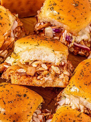 Easy Chicken Sliders with shredded chicken, coleslaw, and herb-topped buns are served on a wooden board—perfect for your next party.