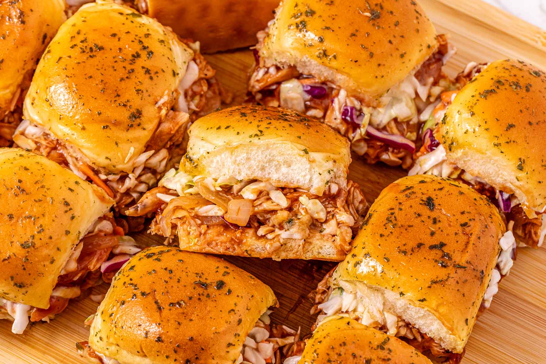 Easy Chicken Sliders with shredded chicken, coleslaw, and herb-topped buns are served on a wooden board—perfect for your next party.