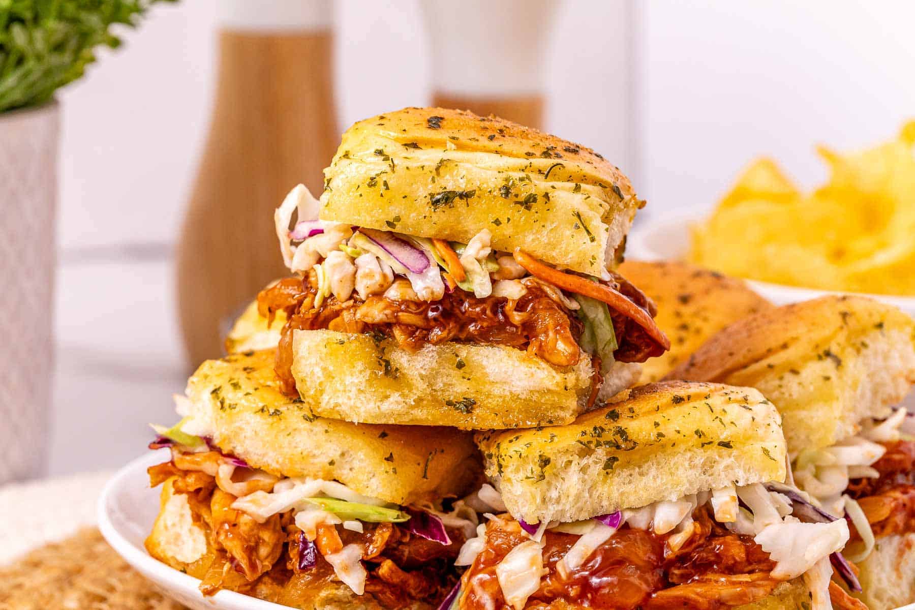 Three Easy BBQ Sliders topped with coleslaw on golden buns, stacked neatly on a white plate.