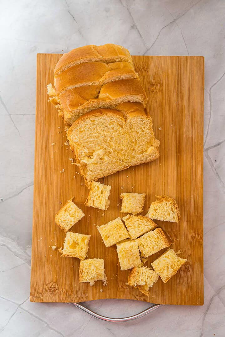 Sliced bread and cubed bread pieces on a wooden cutting board, set on a marble surface&mdash;perfect for preparing Eggnog French Toast or a cozy French Toast Casserole.