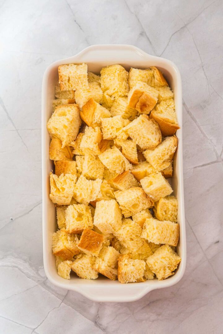 Cubed bread pieces arranged in a white rectangular baking dish on a marble countertop, ready to be transformed into a delicious Eggnog French Toast Casserole.