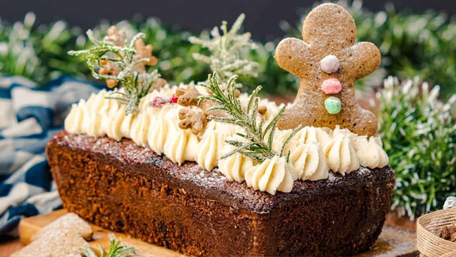 A festive loaf cake topped with icing, rosemary sprigs, and gingerbread men decorations.