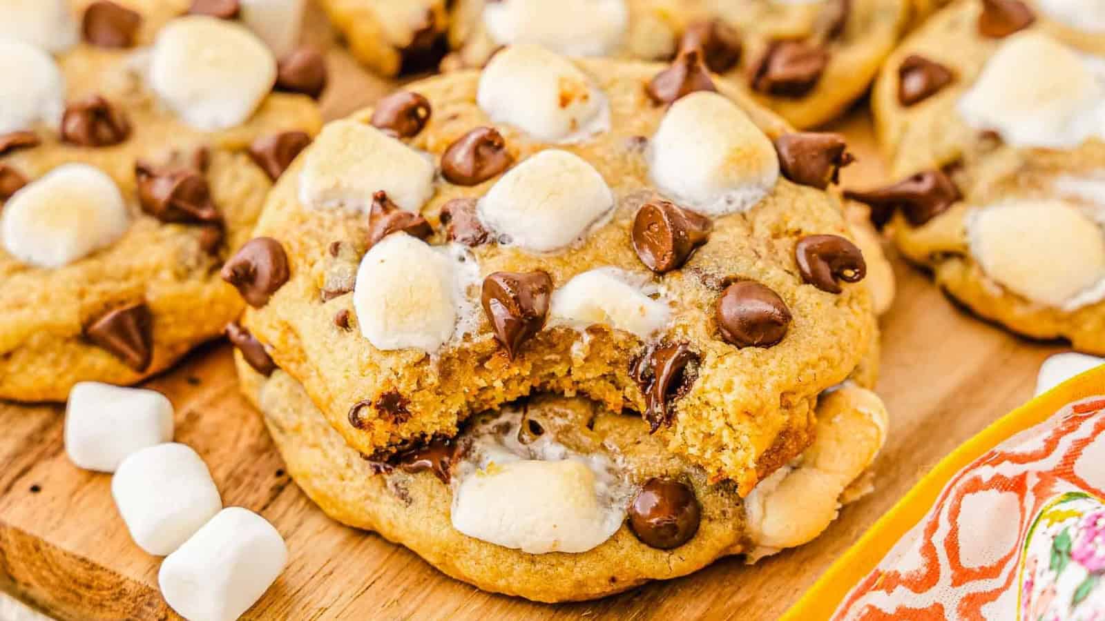 A gooey cookie with chocolate chips and mini marshmallows, with a bite taken out, on a wooden board.