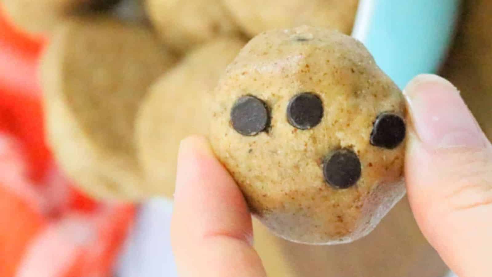 Paleo cookie dough ball being held between fingers with more in a bowl.