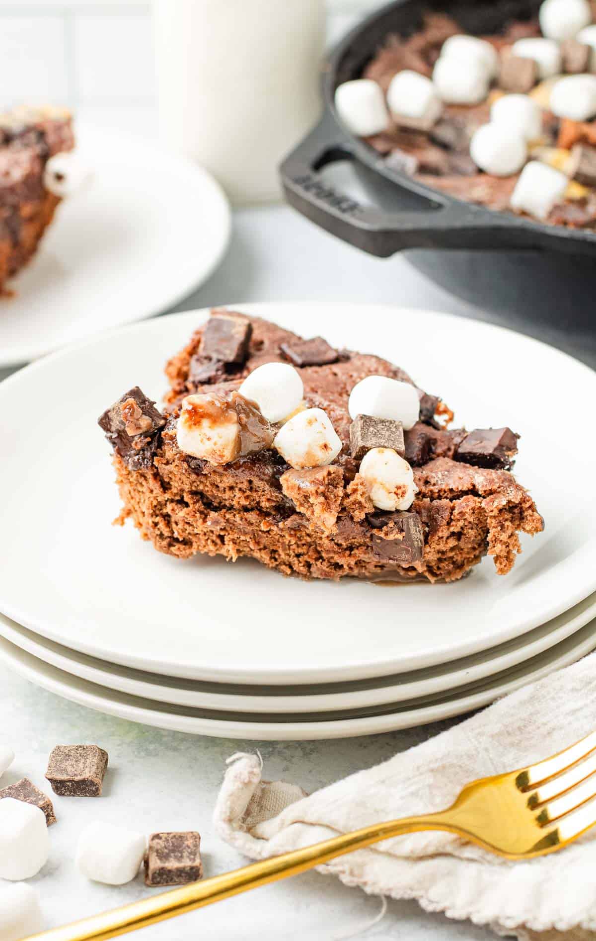 A slice of chocolate dessert inspired by a Hot Chocolate Cobbler, topped with marshmallows and chocolate chunks on a white plate.