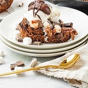 A slice of brownie topped with vanilla ice cream, chocolate drizzle, and marshmallows on a stack of plates—this irresistible treat is inspired by a classic Hot Chocolate Dessert.