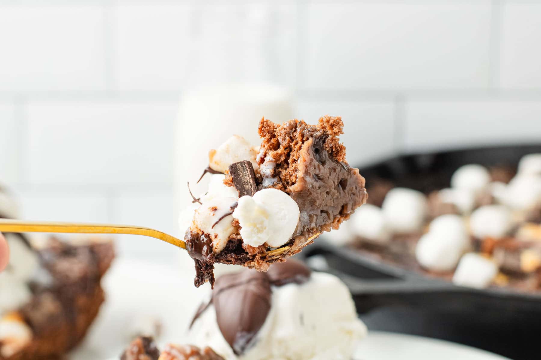A fork holds a gooey Hot Chocolate Cobbler dessert with marshmallows and chocolate chunks above a plate.