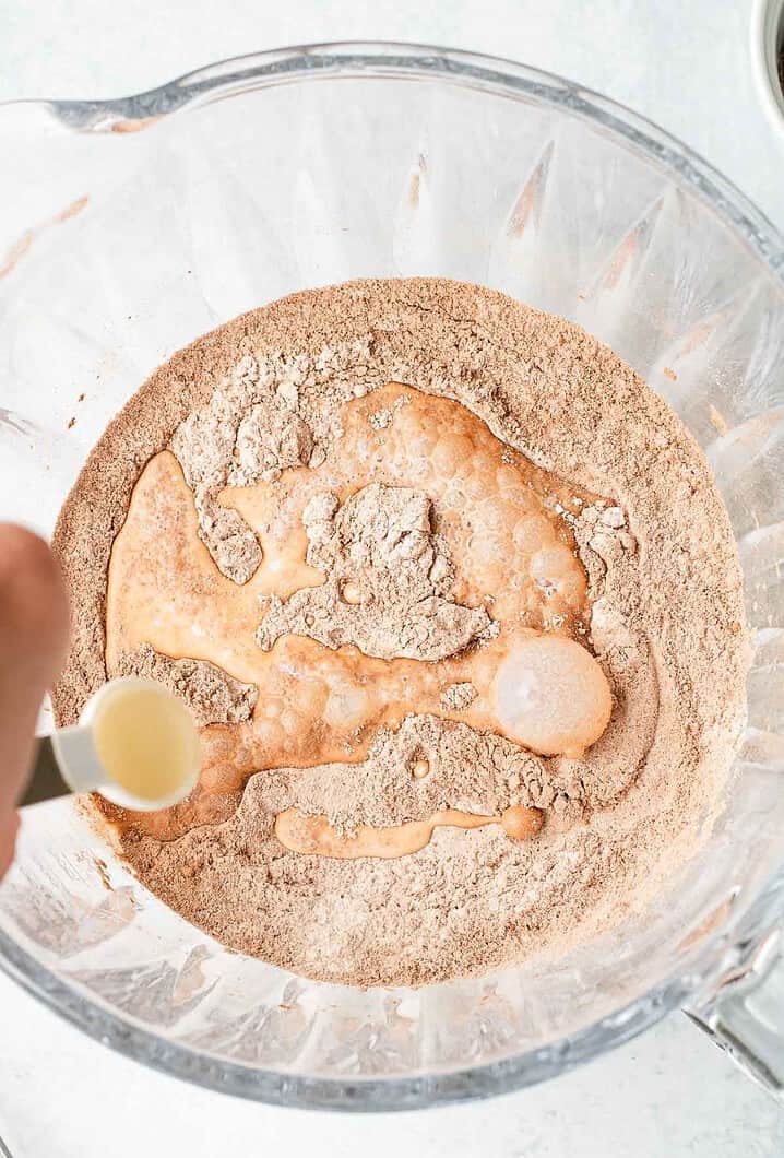 A hand pours liquid into a bowl of cocoa powder and flour mixture for baking this delicious Hot Chocolate Cobbler recipe.
