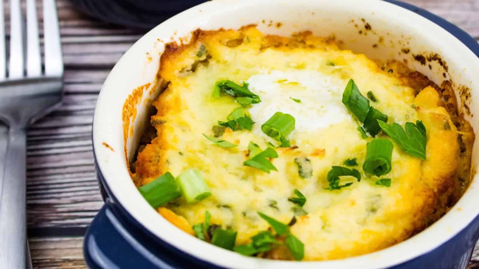 A baked casserole topped with melted cheese and chopped green onions in a round dish on a wooden table.
