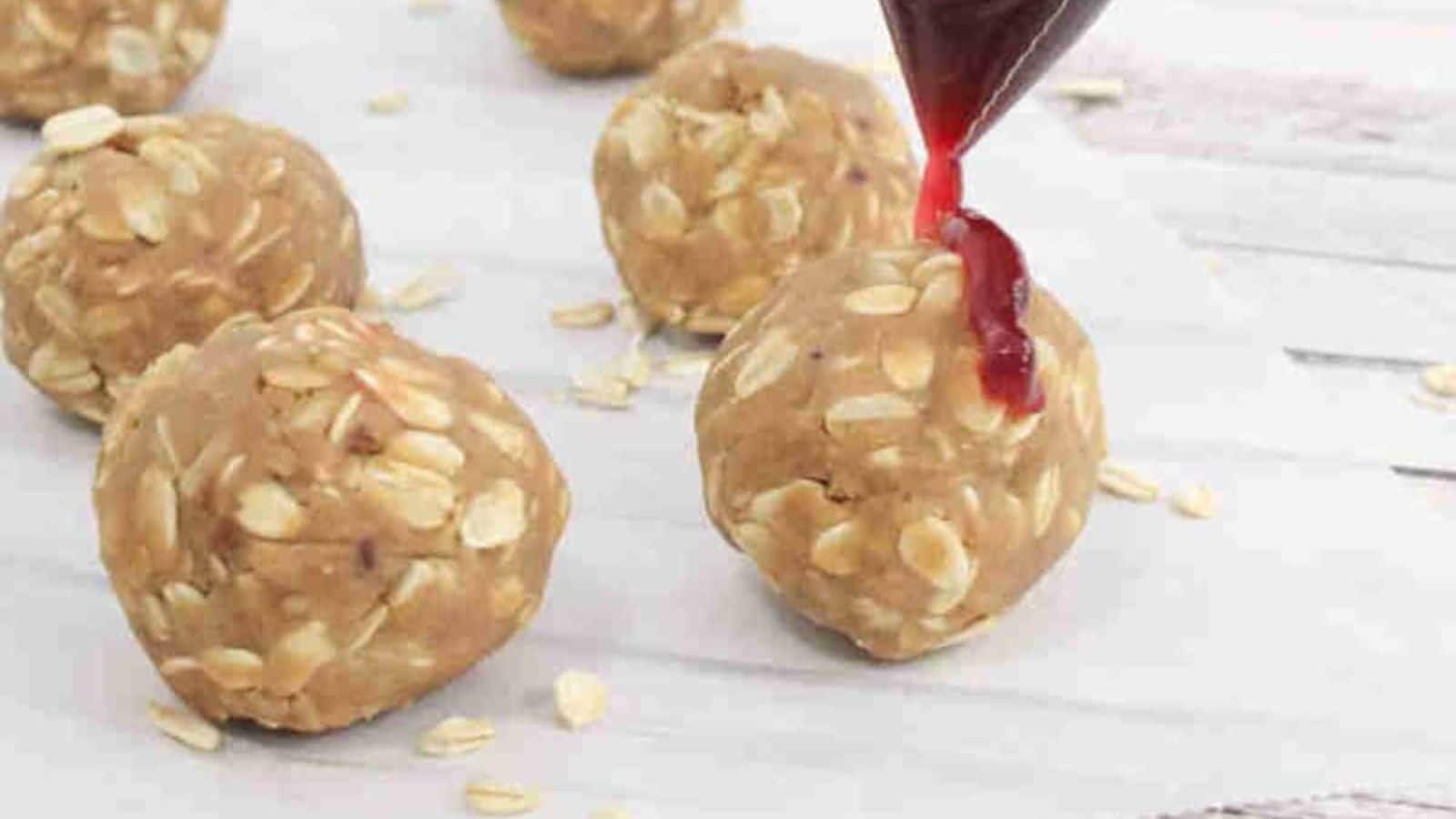 Peanut butter and jam protein balls drizzled with jam on parchment paper.